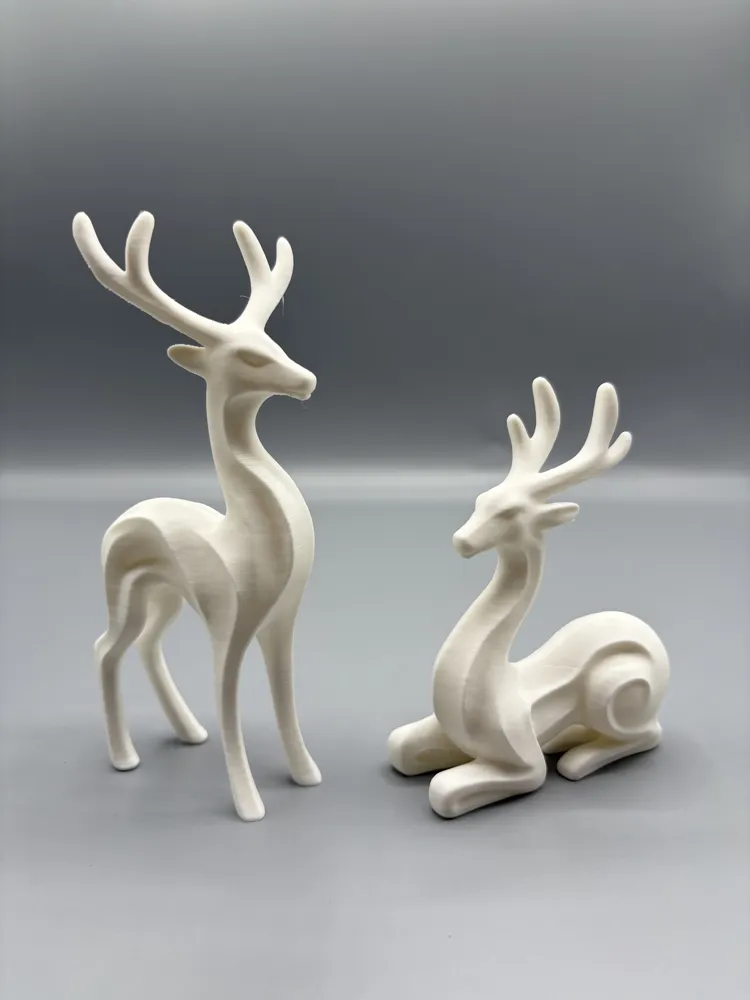 Minimalist Reindeer Pair Display Set — example colour. Includes: Two printed reindeer figures: one standing and one seated; display accessories excluded. Approximate dimensions (Width × Depth × Height): 1 supplied: 64.2 × 46.2 × 139.7 mm; 1 supplied: 75.3 × 50.5 × 101.2 mm.