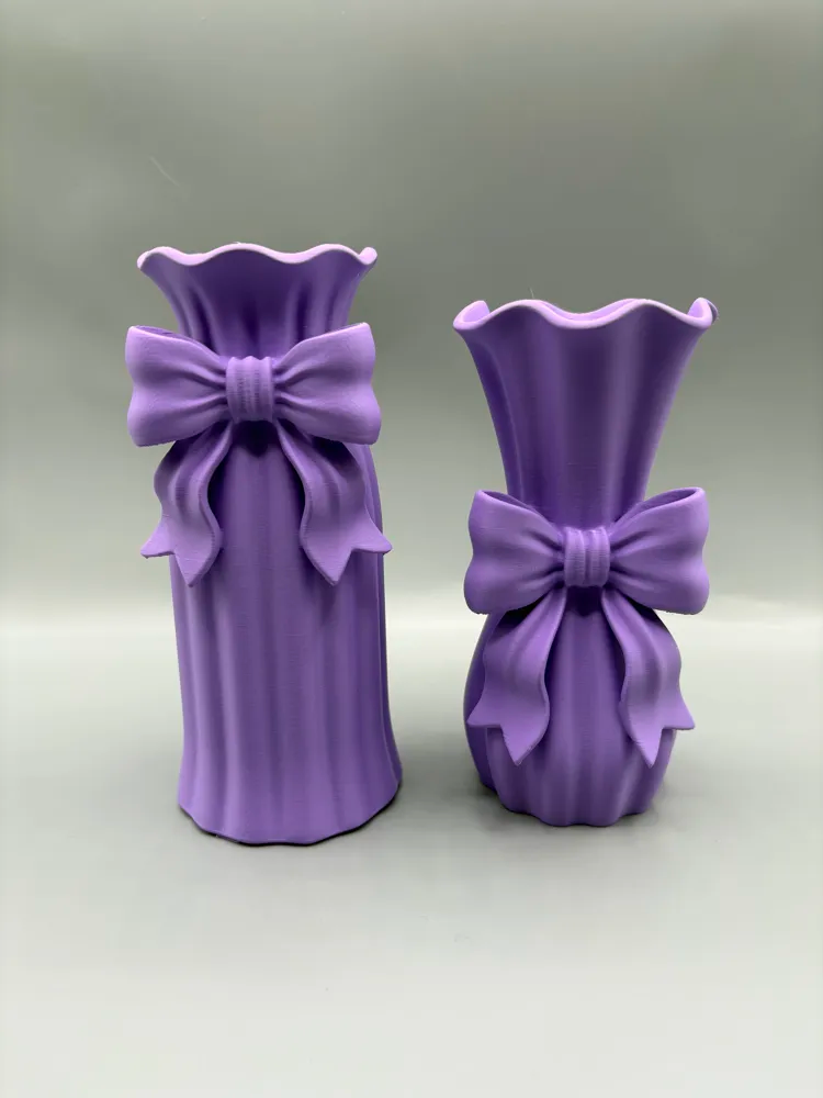 Ribbon Bow Decorative Vase Duo — example colour. Includes: Two printed decorative vases: one tall and one petite; flowers and display accessories excluded. Approximate dimensions (Width × Depth × Height): 1 supplied: 75.7 × 73.6 × 169.4 mm; 1 supplied: 78.7 × 76.5 × 154.9 mm.