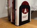 Minimalist Bookend Stand — example colour. Includes: one minimalist bookend stand. Approximate dimensions (W × D × H): • Minimalist Bookend Stand: 110 × 90 × 135 mm.