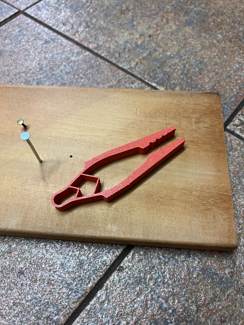 Red 3D-printed nail holder with example nails on a wooden board