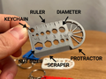 Ruler & Scraper Multi-Tool Keyring — example colour. Includes: one ruler & scraper multi-tool keyring. Approximate dimensions (W × D × H): • Ruler & Scraper Multi-Tool Keyring: 60 × 35 × 3 mm.